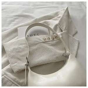 Detail shot of a minimalist cream hobo underarm bag on a white textured fabric background