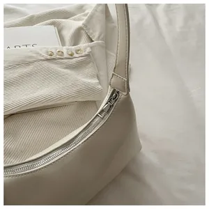 Macro detail view of a cream white underarm hobo bag showing zipper and leather texture