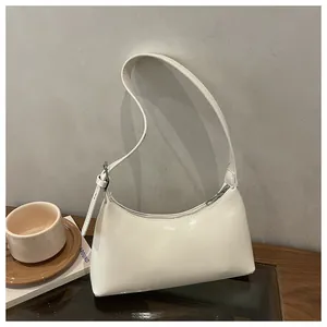 Minimalist white underarm bag with glossy finish and buckle strap on a wooden table