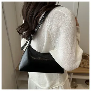 Close-up of a black shiny faux leather underarm bag featuring silver grommet strap