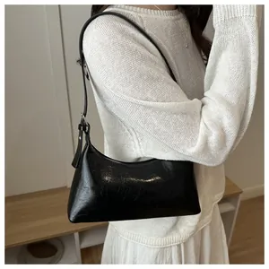 Detail of a black textured baguette shoulder bag worn over a minimalist white knit sweater