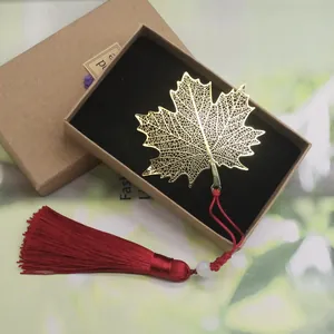 Detailed gold brass maple leaf bookmark with a red tassel in a kraft gift box for readers.