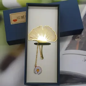Detailed view of a gold ginkgo leaf metal bookmark placed in a premium blue gift box