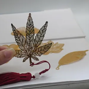 Detailed view of brass filigree maple leaf bookmark with red tassel and bead.