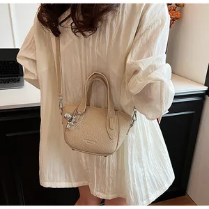 Close-up of minimalist beige litchi grain handbag with cute bear keychain.