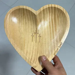 Close-up detail of a heart-shaped wooden prayer bowl featuring engraved crosses and text