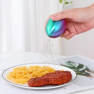 Hand using iridescent egg-shaped stainless steel seasoning shaker over a steak plate
