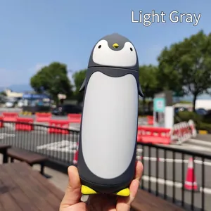 Creative light grey penguin-shaped cartoon glass water bottle shown in a hand outdoors