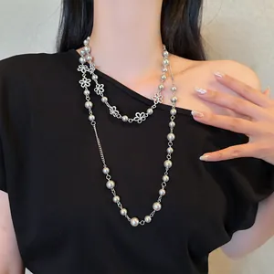 Detail view of a punk-style long necklace with pearls and flower motifs on a model.