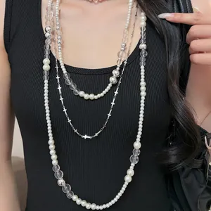 Detailed close-up showing a layered long necklace featuring pearls, clear beads and silver crosses.