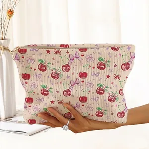 Detailed view of the cherry and bow pattern print on a beige corduroy makeup bag.