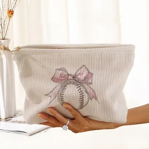 Macro view of a cream corduroy makeup bag featuring a pink bow and baseball print.