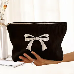 Close-up view of a black corduroy makeup bag featuring a white bow print, held by a hand