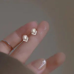 Macro detail of delicate pearl stud earrings with V-shaped crystal setting on a finger