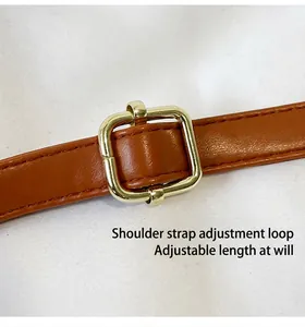 Close-up of the adjustable gold buckle on the brown leather shoulder strap of the bag