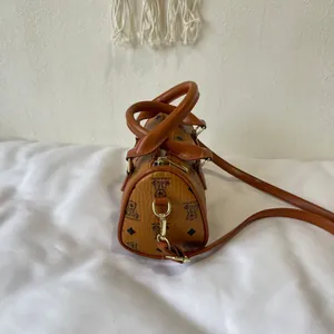 Close-up side view of a brown luxury barrel bag featuring cute bear prints and a long strap