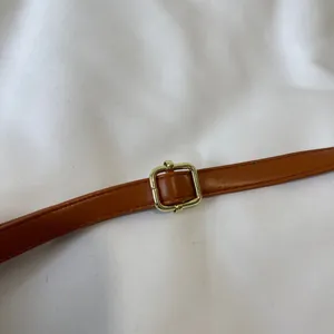 Close-up detail of the adjustable cognac brown leather shoulder strap with gold metal buckle