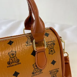 Close-up of brown textured leather handbag with cute bear pattern and gold hardware.