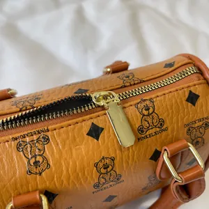 Macro view showing the high-quality golden zipper and bear print on a brown leather barrel bag
