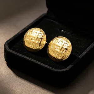 Detail of gold stainless steel stud earrings featuring a textured grid pattern