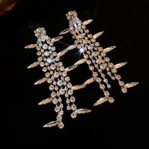 Macro shot of silver needle tassel earrings with sparkling rhinestones on black background.