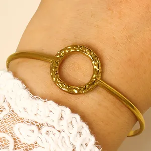 Detailed macro view of a golden open cuff bracelet featuring a hammered circle charm