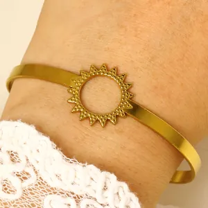 Close-up detail of a minimalist gold sun-shaped open bangle bracelet on the wrist.