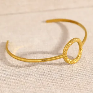 Close-up detail shot of golden open cuff bracelet with hammered texture circle element