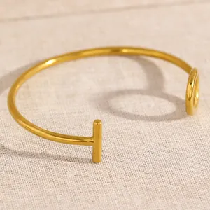 Detail of a minimalist gold-plated stainless steel open cuff bracelet with T-bar