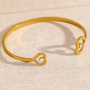 Close-up detail of a minimalist gold-toned open bangle featuring heart-shaped crystal ends