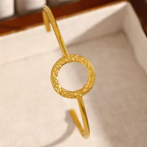 Detailed view of minimalist gold open cuff bangle with a textured circular center