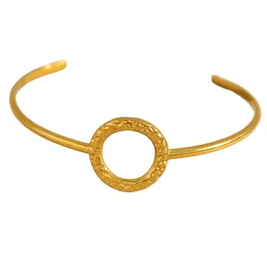 Detail of a minimalist gold cuff bracelet featuring a textured hammered circle element.