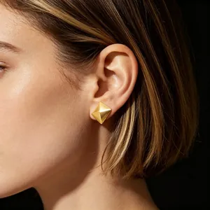 Close-up detail of a minimalist gold geometric pyramid stud earring worn on model ear
