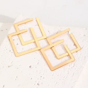 Detailed view of gold-plated irregular geometric square earrings on a textured stone.