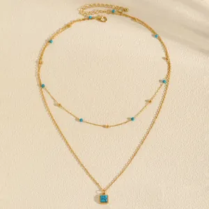 Close-up of bohemian double-layered gold necklace with square turquoise pendant.