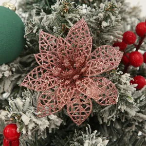 Detail view of rose gold glitter hollow poinsettia flower on a snowy Christmas tree branch
