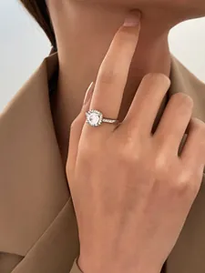 Close-up of a sparkling round zircon halo ring on a female finger wearing a blazer