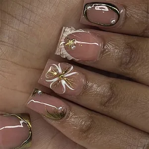 Close-up detail of French style press-on nails with gold accents and pearl decorations.