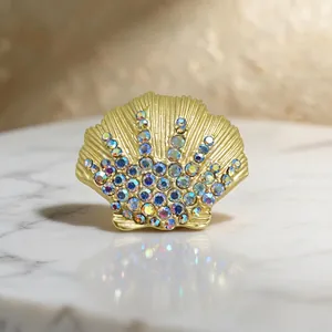 Detailed close-up of a matte gold shell brooch with sparkling iridescent crystals