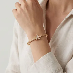 Primo piano di un elegante bracciale rigido a stella marina dorata con cristalli scintillanti.