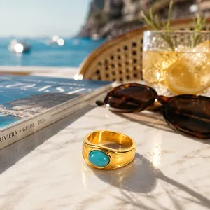Vintage gold stainless steel ring with an oval turquoise stone on a sunny seaside table.