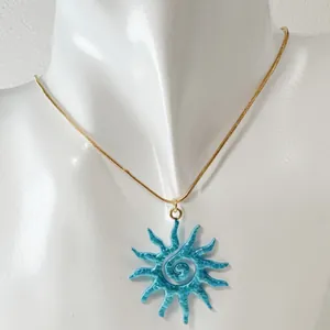 Gros plan d'un pendentif soleil spirale bleu vibrant sur une fine chaîne en or dorée