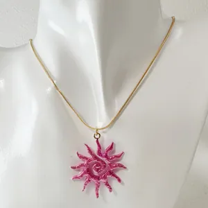 Zoom sur un collier avec pendentif soleil en spirale rose sur un buste de mannequin.