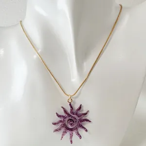 Détail d'un pendentif soleil évidé violet avec un motif en spirale sur chaîne dorée