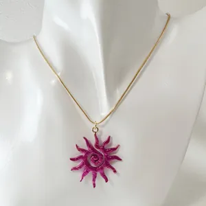 Détail du collier avec pendentif soleil ajouré et spirale magenta sur chaîne dorée.