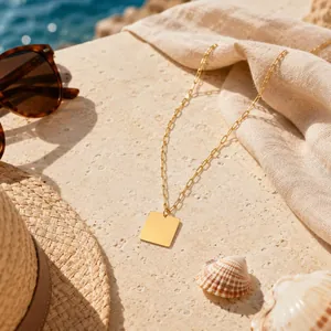 Gros plan d'un collier pendentif carré en acier inoxydable doré sur fond de plage