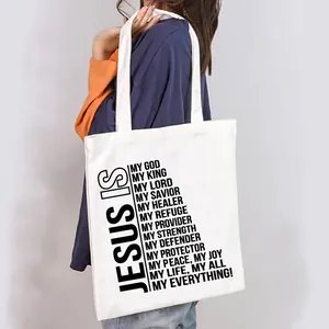 Close-up of a white canvas shopping tote bag featuring a religious 'Jesus Is' quote.