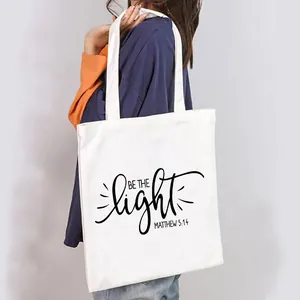 Minimalist white canvas tote bag for women featuring a decorative Be the Light print