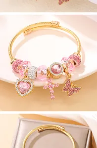 Gros plan d'un bracelet doré avec des breloques roses en forme de cœur, croix et papillon.