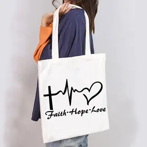 Casual white canvas tote bag with black Faith Hope Love graphic print worn on shoulder